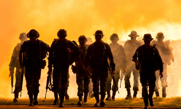 silhouette of unrecognized soldiers with rifle walk through smoke