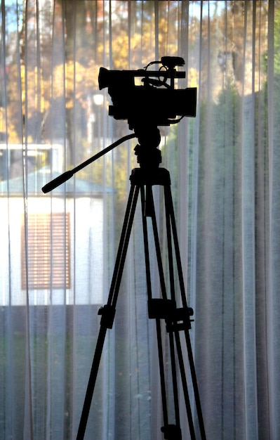 Silhouette Of Video Camera On A Tripod Over Window