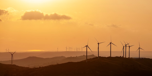 Silhouette of wind turbine wind farm generating renewable energy on sunset