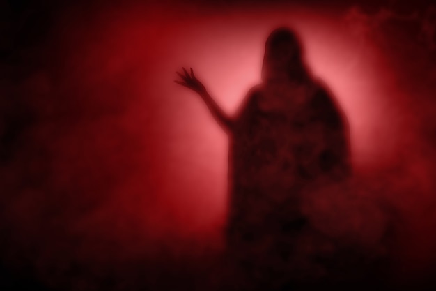 Silhouette of witch woman with a cloak standing with dramatic background