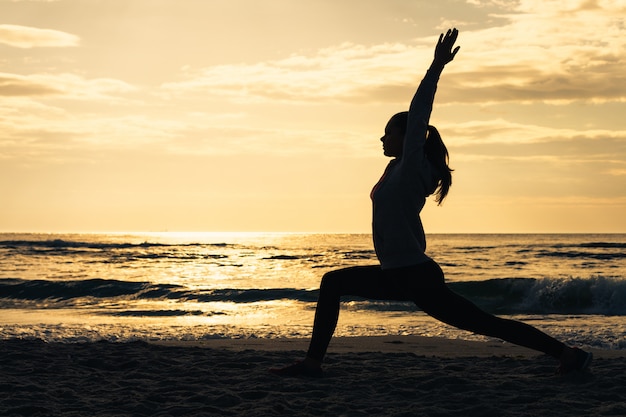 Silhouette of a woman on the beach during morning exercises at sunrise