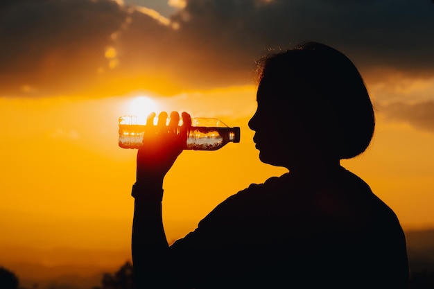 Silhouette of a woman drinking water drinking water in the sunset