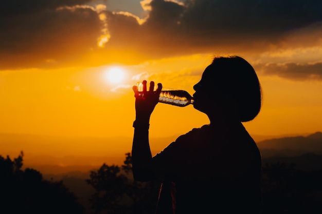 Silhouette of a woman drinking water drinking water in the sunset