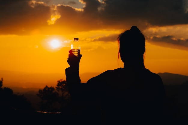 Silhouette of a woman drinking water drinking water in the sunset