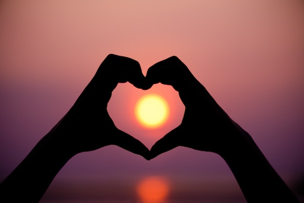 Silhouette the woman hands to be heart shape on sunset background.