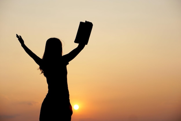 Silhouette of a woman holding a computer sunset background