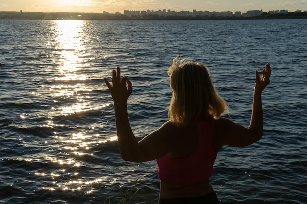 Silhouette of a woman holding her fingers in a mudra pose against the background of the water of the sea lake