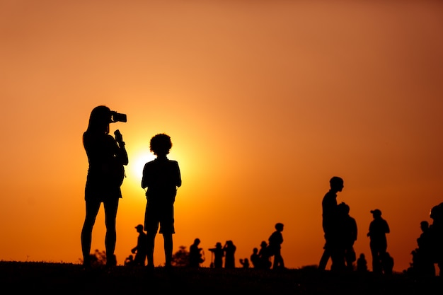 silhouette of a woman holding a smartphone taking pictures with child and crowd people