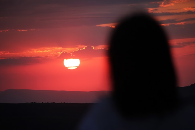 Silhouette of a woman looking at a red sunset Young woman in sunset light looking far away