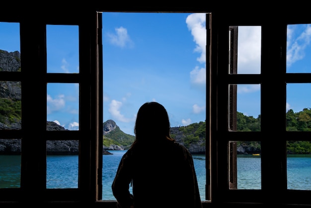 The silhouette of a woman looking through the window with sea views.