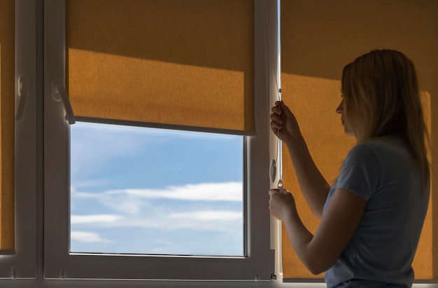 Silhouette of a woman opening the blinds on a sunny morning