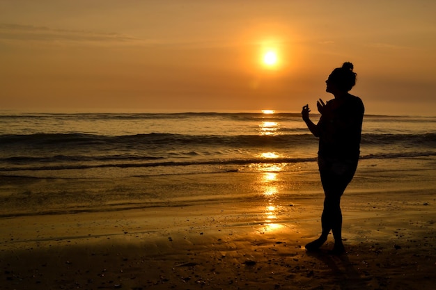 Silhouette of woman playing with hands at sunset on a beach