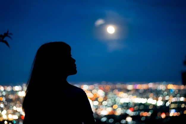 Silhouette Woman portrait with full moon in city night light bokeh background