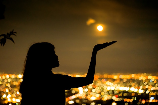 Silhouette Woman portrait with full moon in city night light bokeh background