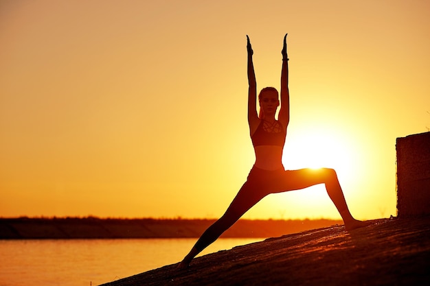 Silhouette woman practicing yoga or stretching on the beach pier at sunset or sunrise