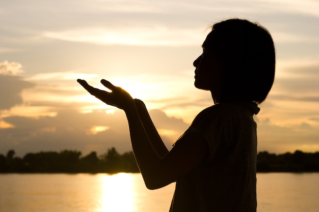 Silhouette of woman praying over beautiful sunset background.