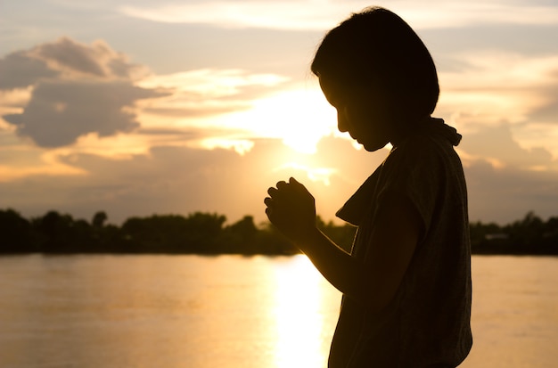 Silhouette of woman praying over beautiful sunset background.