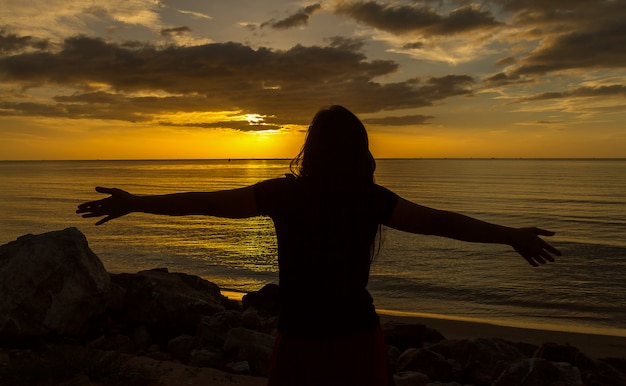 Silhouette of woman praying over beautiful sunset background