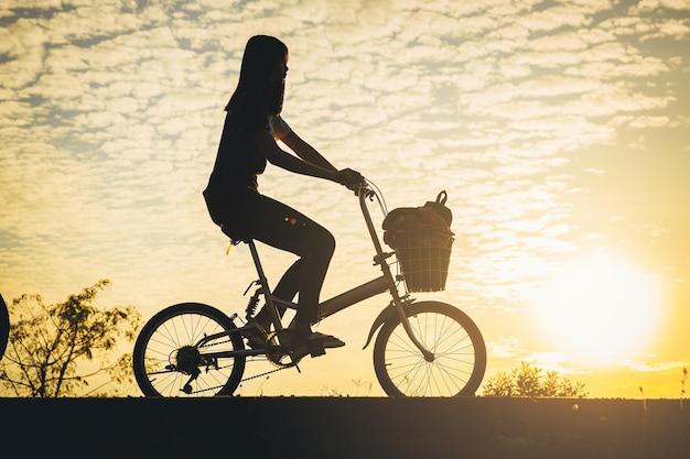 Silhouette of woman ride a bicycle along the bike lane in the park at the sunset.