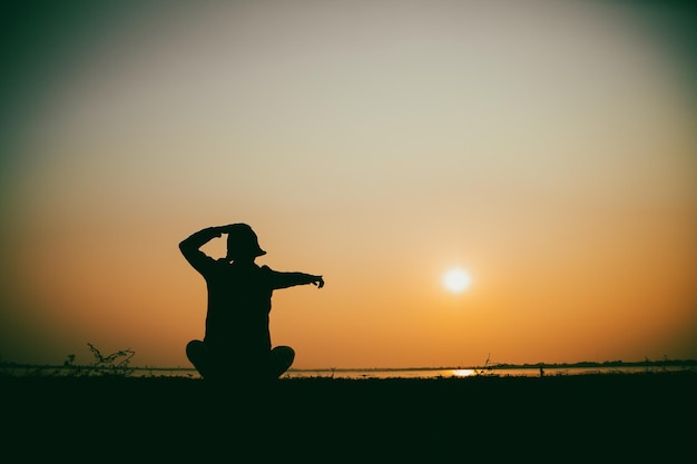 Silhouette of the woman sitting sad at the river during sunset