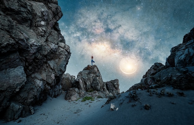 Silhouette of a woman standing in yoga tree position on the rock or mountain with Milky Way