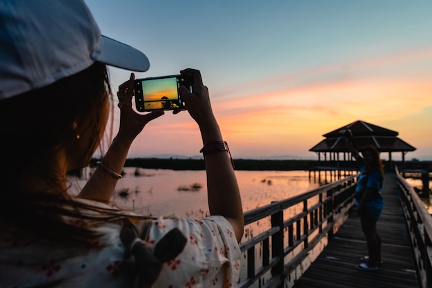 Silhouette of woman taking picture of her friend standing on wooden bridge on sunset in Khao Sam Roi Yot National Park. Thailand.