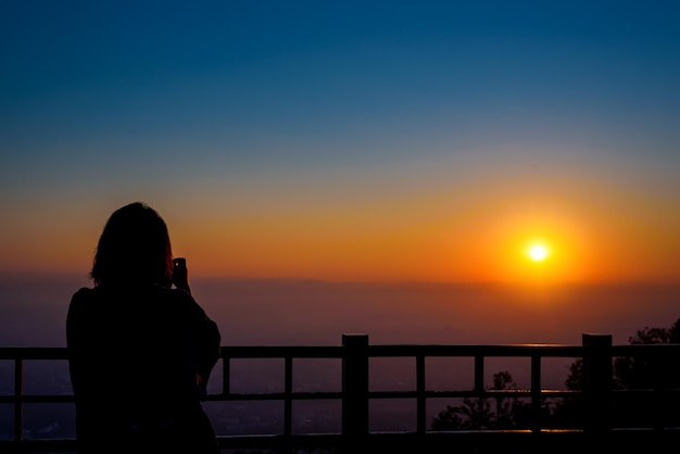 silhouette of  woman taking picture with camera at sunrise on DOI SUTHEP mountain viewpoint, chiang mai, Thailand