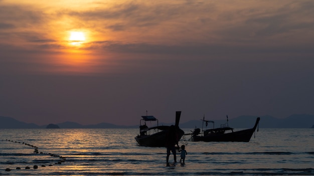 Silhouette of  woman with a child walk in the sea on the background of sunset by the sea