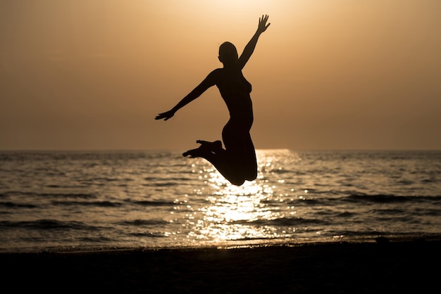 Silhouette of Woman With Raised Hands And Jumping Around on the Beach at Sunset  Copy Space Text