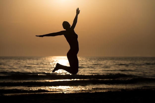 Silhouette of Woman With Raised Hands And Jumping Around on the Beach at Sunset  Copy Space Text