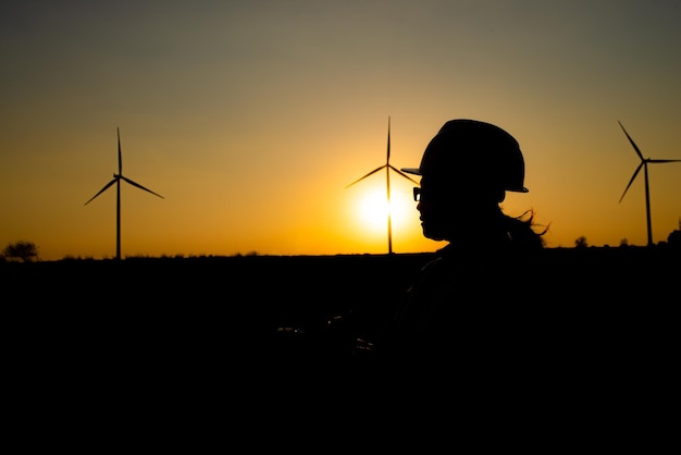 Silhouette of women engineer working and holding the report at wind turbine farm Power Generator Station on mountainThailand people