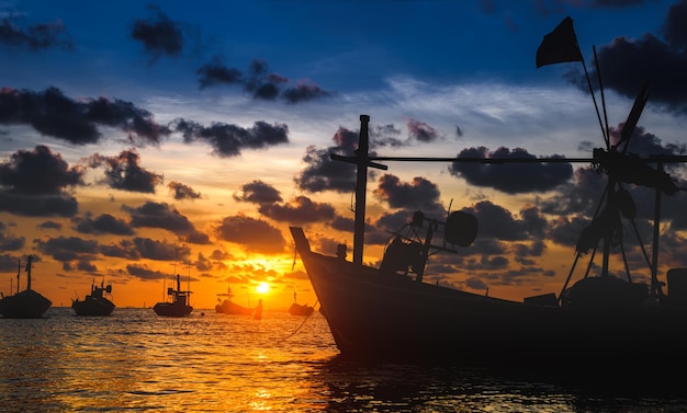 Silhouette wooden fishery boats in the sea with sunset twilight lighting.