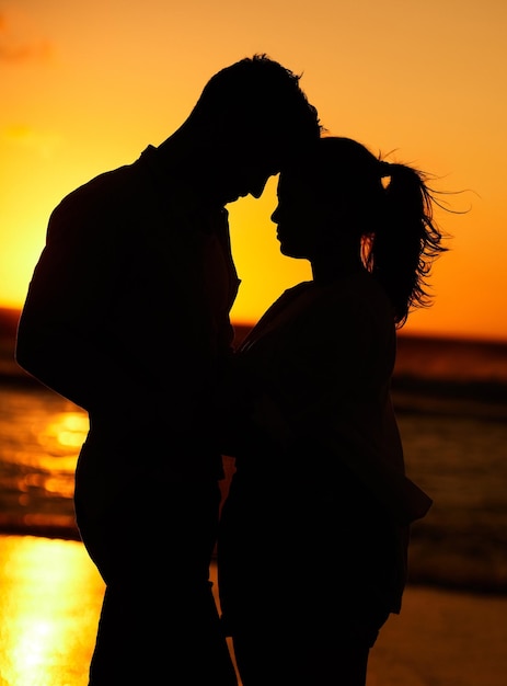 Silhouette of young couple on the beach at sunset embracing each other in affection People on holiday vacation and honeymoon by the ocean Intimate love and romantic man and woman together by sea