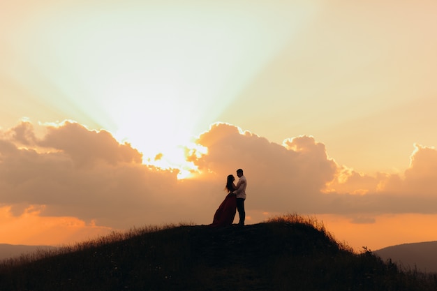 silhouette of a young couple in love at sunset, they embrace kiss and look at each other with tenderness. Slow motion. Young couple at sunset.