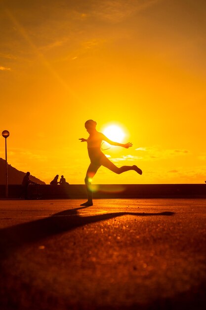 Silhouette of a young female dancer performing a jump along the beach at sunset