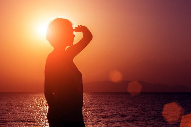 Silhouette of young girl looking into the distance standing on the beach at the sunset against the sun