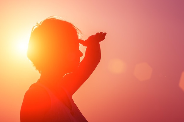 Silhouette of young girl looking into the distance standing on the beach at the sunset against the sun