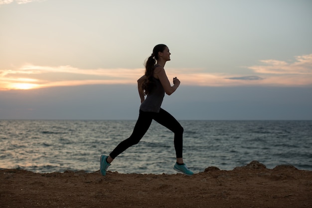 Silhouette of a young girl running along the beach of the sea during an amazing sunset.