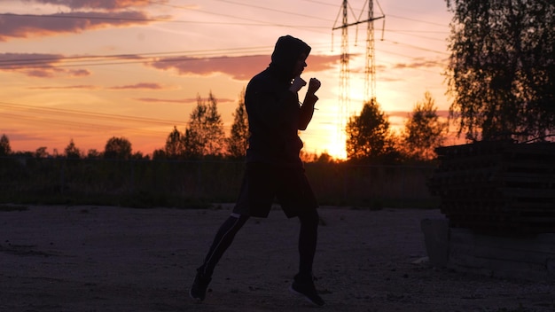 Silhouette of young man boxer training for kicking on sunset at city park