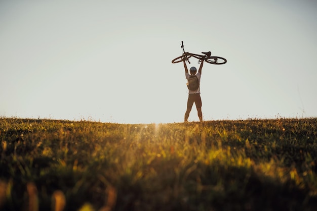 Silhouette of a young man holding a bicycle in the field at sunset with a dramatic sky in the background Highquality photo