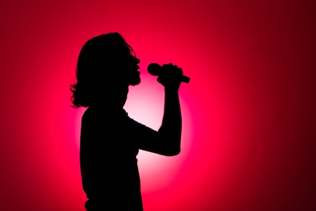 Photo silhouette of young man holding wireless microphone and singing music with emotion