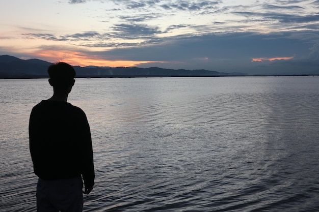 Silhouette of a young man standing by the lake enjoying the sunset. peaceful atmosphere in nature