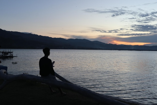 Silhouette of a young man standing by the lake enjoying the sunset. peaceful atmosphere in nature