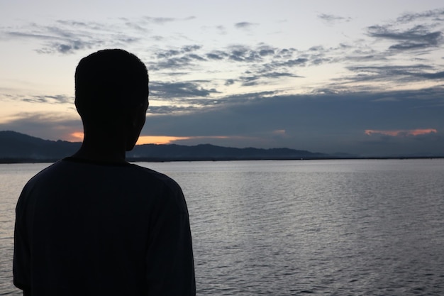 Silhouette of a young man standing by the lake enjoying the sunset. peaceful atmosphere in nature