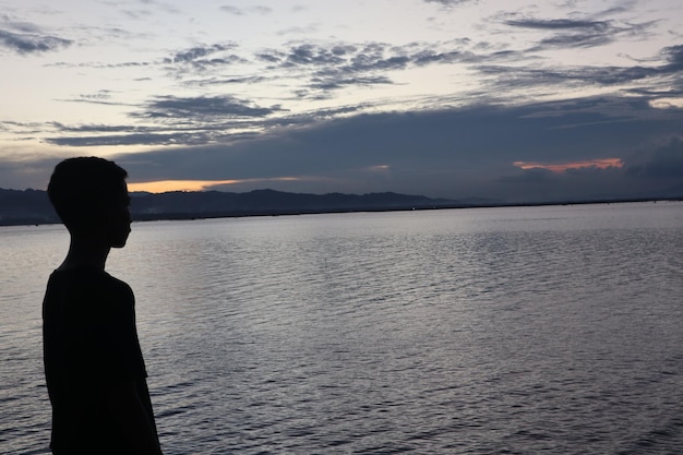 Silhouette of a young man standing by the lake enjoying the sunset. peaceful atmosphere in nature