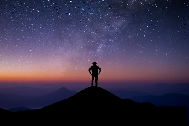 Silhouette of young man standing on top of mountain watching beautiful night sky star and milky way.