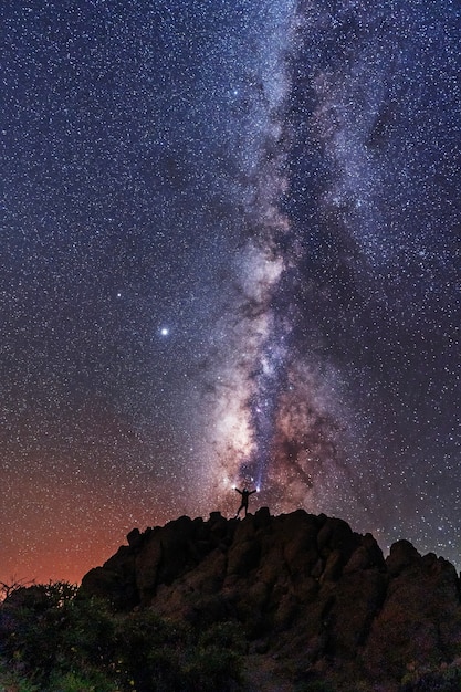 Silhouette of a young man under the stars looking at the milky way at night, astrophotography