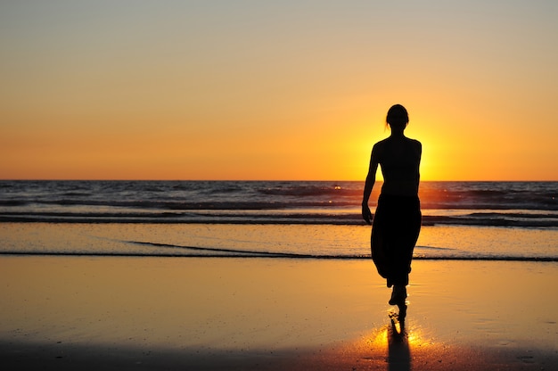 Silhouette of young woman against sunset by the sea. Figure of a woman in the rays of setting sun. Beautiful sunset, touchdown and a girl walking on seashore