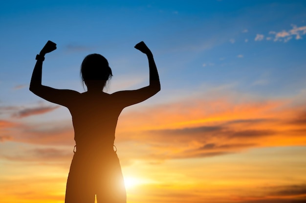 Silhouette of young woman open both arms standing and watched beautiful view sunset alone on top of the mountain She enjoyed traveling and was successful when he reached the summit