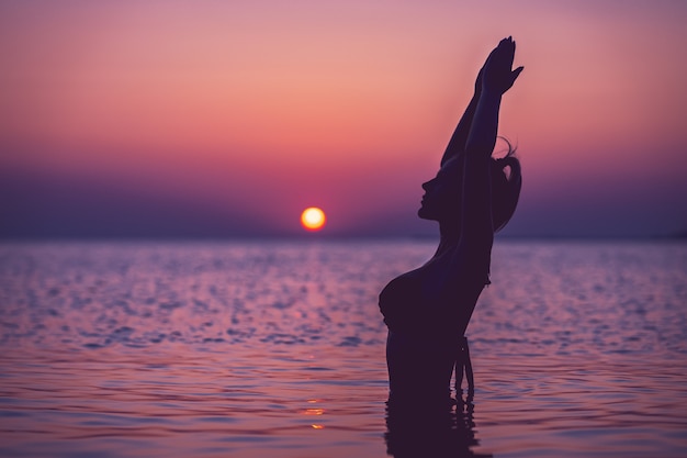 silhouette of young woman practicing yoga on the beach at sunrise